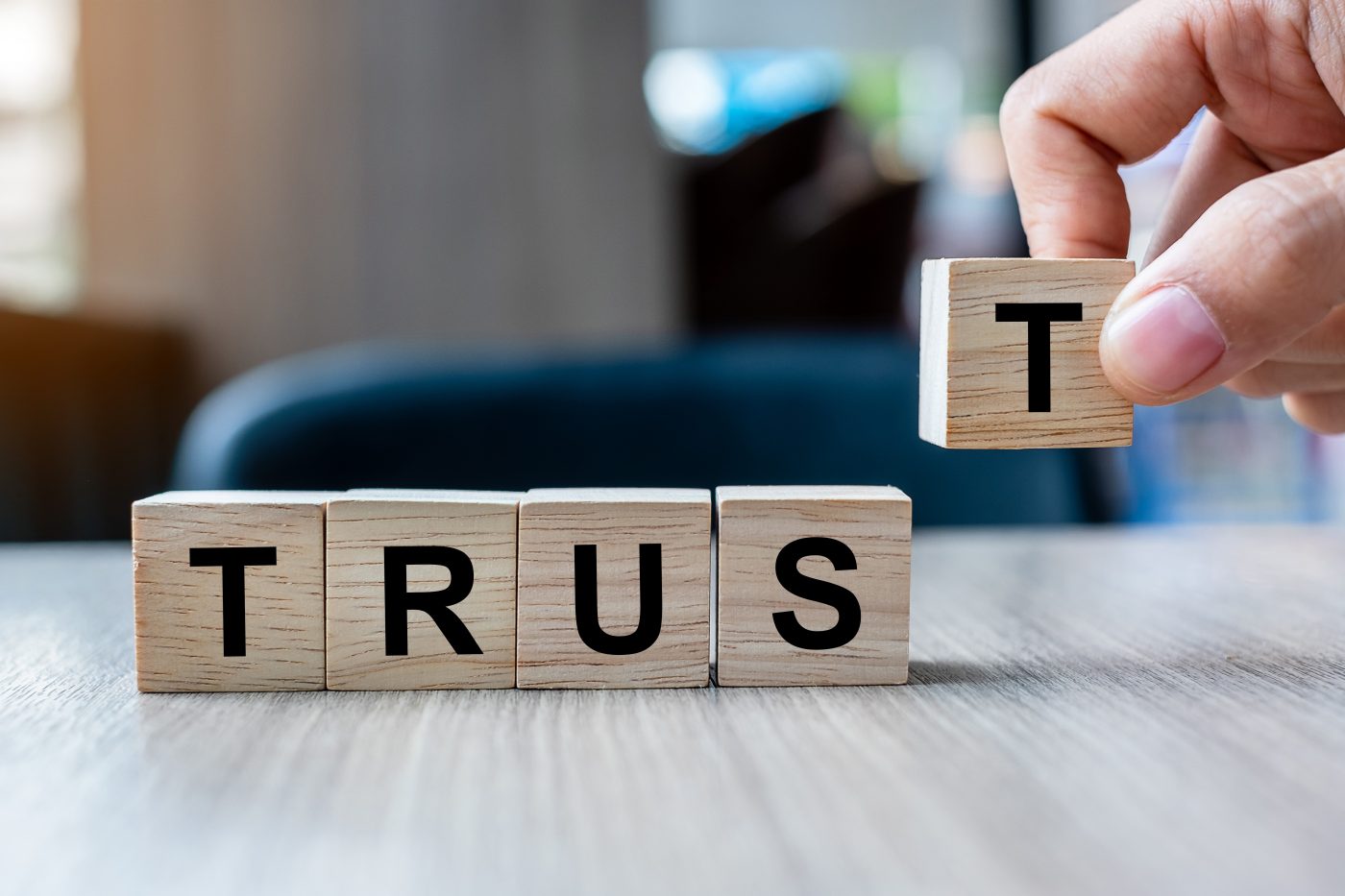 Businessman hand holding wooden cube block with TRUST business word on table background. Trustworthy, Truth, beliefs and agreement concept